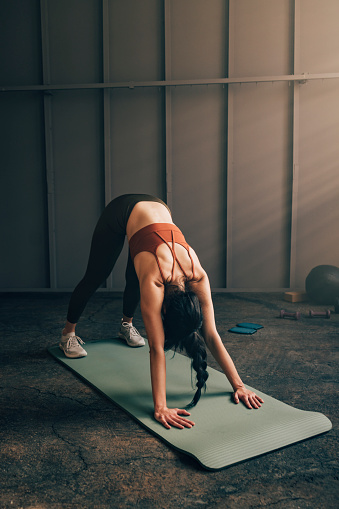 An unrecognizable white woman doing yoga on a mat, holding a downward dog pose.
