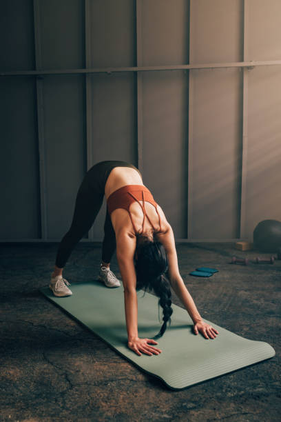 Anonymous Caucasian Woman in a Downward Facing Dog Position on a Yoga Mat An unrecognizable white woman doing yoga on a mat, holding a downward dog pose. yoga studio photos stock pictures, royalty-free photos & images
