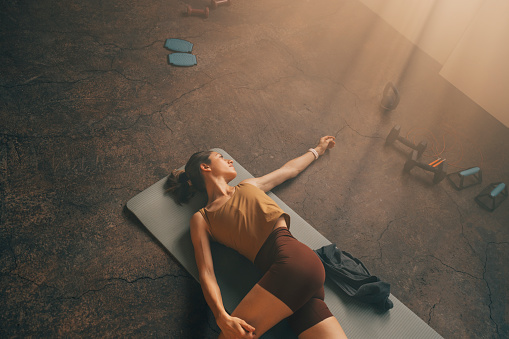 A fit Caucasian woman lying on a yoga mat and stretching after exercising at the gym.
