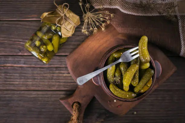 Homemade canning. Marinated cucumbers gherkins with dill and garlic in a glass jar on a dark wooden table. Vegetable salads for winter.