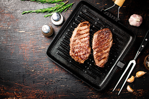 Aromatic grilled steak in a frying pan. Against a dark background. High quality photo