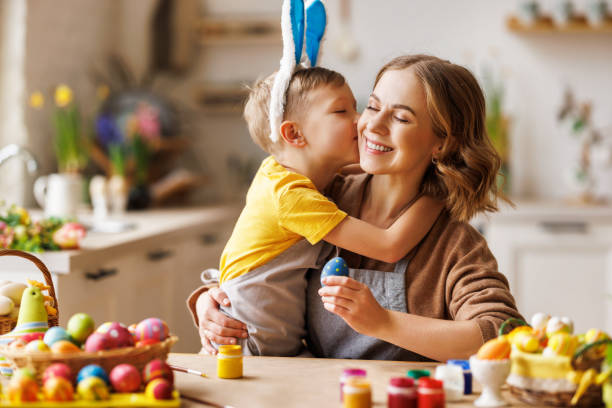 istock Little son kissing and hugging young happy mother while decorating Easter eggs together in kitchen 1375715321