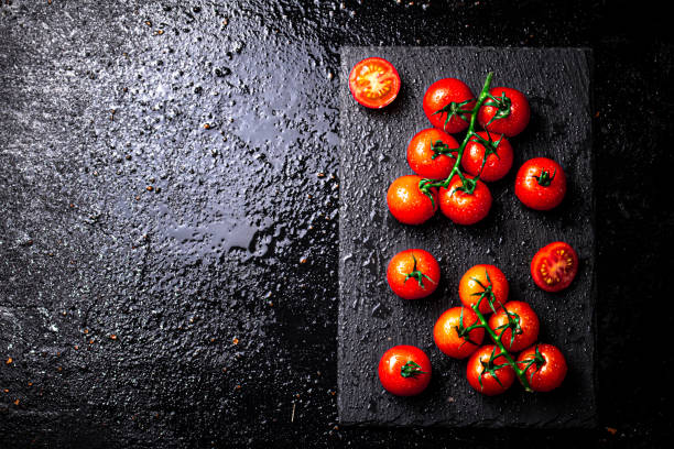 istock Fresh tomatoes on a branch on a stone board. 1375721690