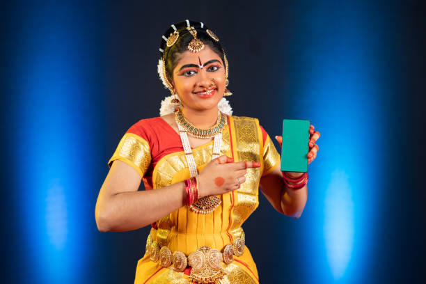 istock Indian bharatanatyam dancer showing green screen mobile phone by pointing finger while looking at camera - concept of app advertisement, promotion and artist. 1375761255