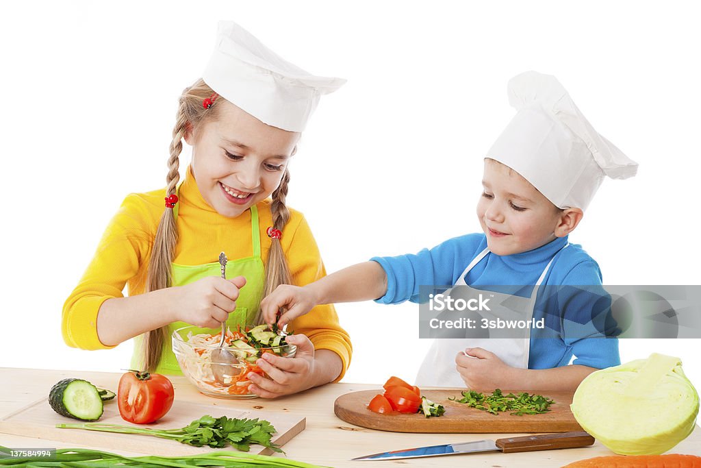 Young girl and boy happily making a salad together Two smiling kids mixing salad, isolated on white Apron Stock Photo