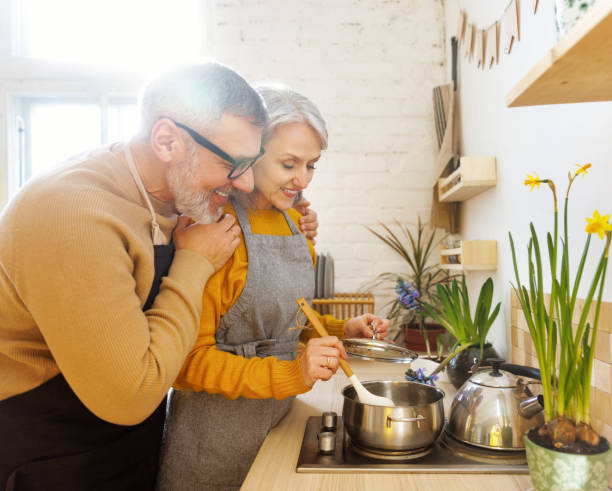 joyeux couple de personnes âgées en tabliers préparant une soupe végétarienne ensemble dans une cuisine confortable - making soup photos et images de collection