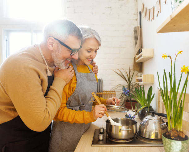 szczęśliwa radosna para seniorów w fartuchach przygotowująca razem wegetariańską zupę w przytulnej kuchni - cooking men caucasian togetherness zdjęcia i obrazy z banku zdjęć