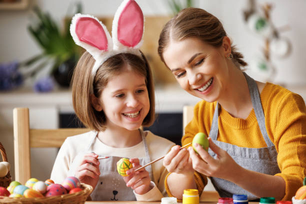 istock Loving young mother teaching happy   kid daughter to decorate Easter eggs while sitting in kitchen 1375876753