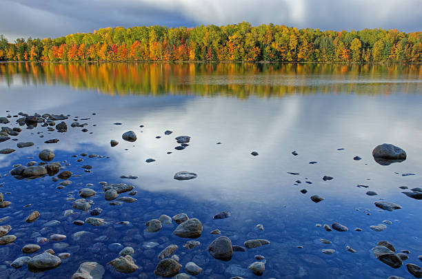 Autumn landscape of Moccasin Lake with reflections of trees in calm water and storm clouds, Michigan's Upper Peninsula, USA
