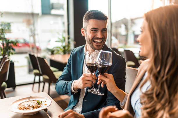 happy couple eating lunch together in a restaurant and toasting with wine. - restaurant imagens e fotografias de stock