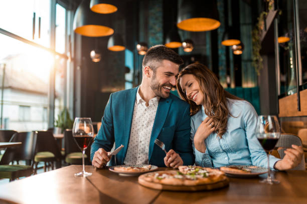 pareja juguetona comiendo pizza juntos en un restaurante. - restaurante fotografías e imágenes de stock