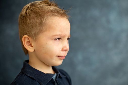 Sad little child, blond toddler boy, crying, image isolated on blue