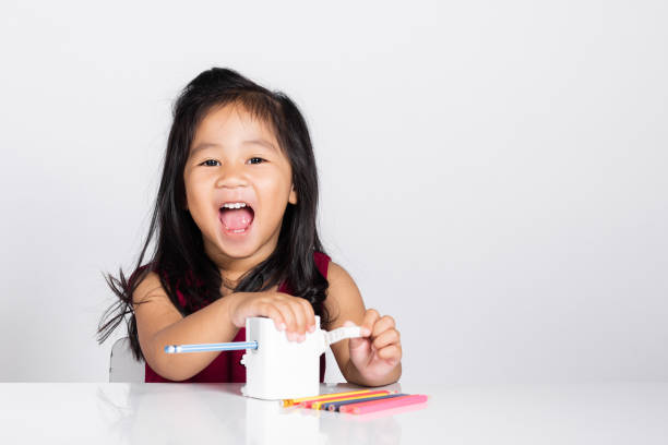 menina bonitinha de 3 a 4 anos sorri usando apontador de lápis enquanto fazia lição de casa em tiro de estúdio isolado - preschool 2 3 years preschooler little girls - fotografias e filmes do acervo