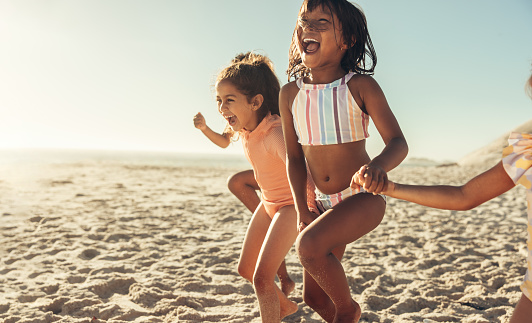 Excited little girls running and having fun together at the beach. Group of happy little children enjoying their summer vacation at a sunny beach.