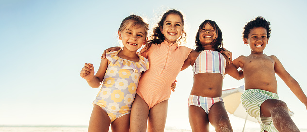 Excited little children smiling happily while standing together at the beach. Group of energetic little children having fun together during summer vacation.