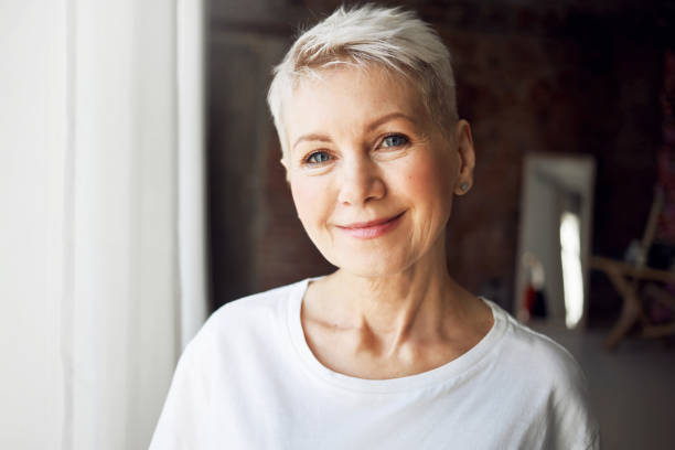 age, beauty, wellbeing and health concept. close up portrait of good looking beautiful mature female with gray pixie hair, blue eyes and wrinkles smiling happily at camera, being in good mood - women smiling blond hair human face imagens e fotografias de stock