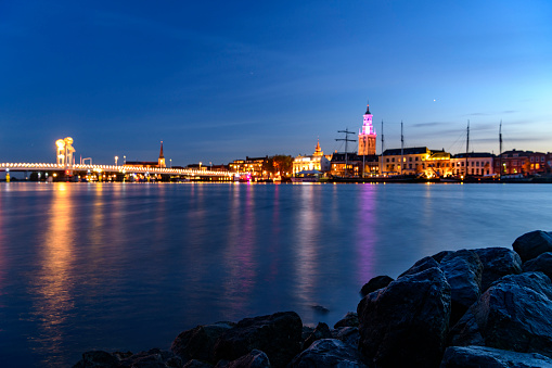 Evening panorama of the skyline with the Stadbrug and Nieuwe Toren of the city of Kampen in Overijssel, The Netherlands. The lights of the city are reflected in the calm water while clouds are moving over the city in the sky.