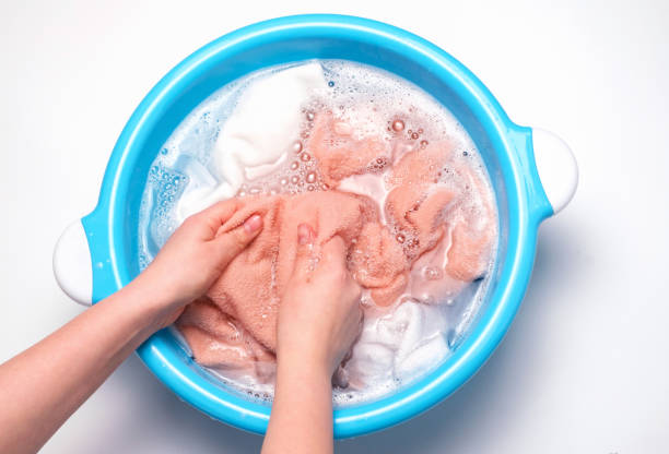 Female hands washing multicolored towels in a basin, top view