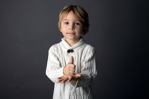 Cute little toddler boy, showing HELP gesture in sign language on gray background, isolated image, child showing hand sing