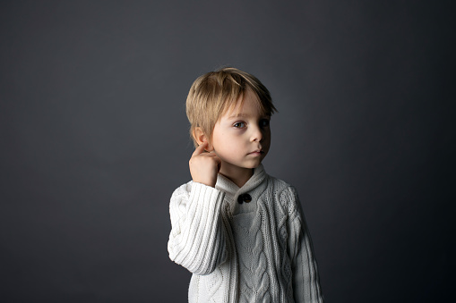 Cute little toddler boy, showing not hearing gesture in sign language on gray background, isolated image, child showing hand sings