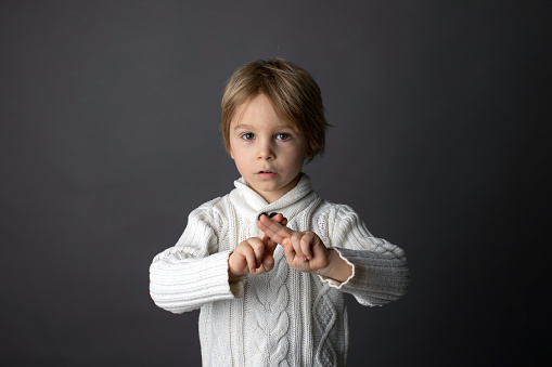Cute little toddler boy, showing gesture in sign language on gray background, isolated image, child showing hand sings