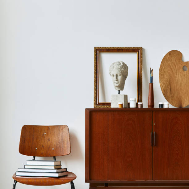 istock Stylish composition of artist workspace room with design retro teak commode, poster frames, easel, book, decoration and painting accessories. Template. 1376038662
