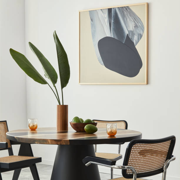 istock Stylish composition of dining room interior with design table, modern chairs, decoration, tropical leaf in vase, fruits, abstract mock up paintings and elegant accessories in home decor. Template. 1376054948