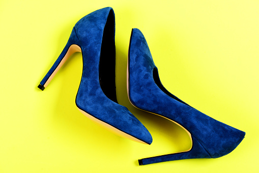 Fashion and beauty concept. Pair of blue suede high heel shoes. Female formal footwear, top view. Elegant blue shoes isolated on yellow background.