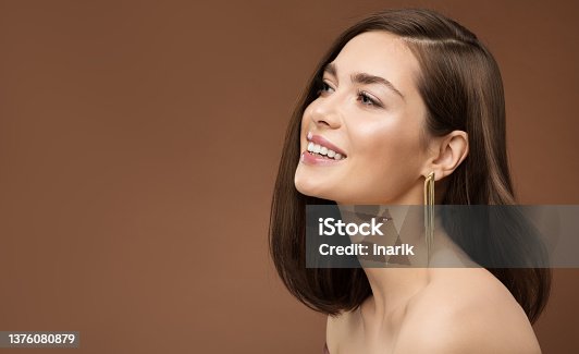 istock Cheerful Smiling Model Profile Side View. Brunette Beauty Woman with Nude Make up Smooth Skin and Golden Earring over Brown Background 1376080879