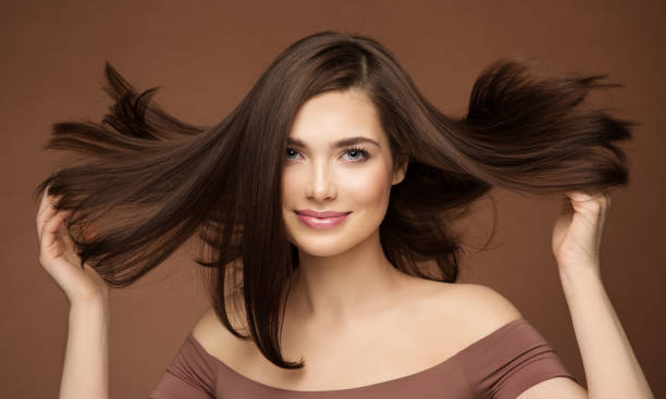 modello di bellezza dei capelli. donna bruna con acconciatura dritta che vola su wind over dark beige. giovane ragazza sorridente con trucco per la pelle liscia - capelli castani foto e immagini stock