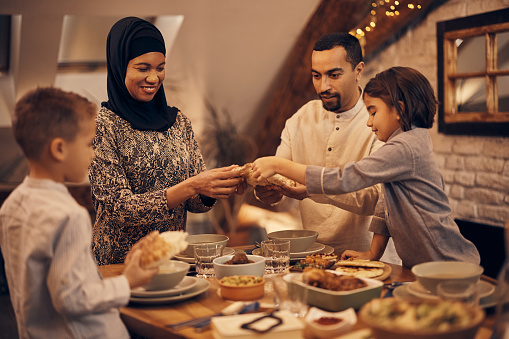 Happy Middle Eastern family sharing pita bread at dining table on Ramadan.