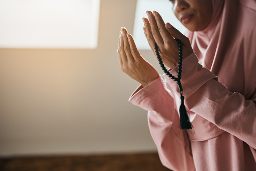 Close-up of Muslim woman using misbaha beads while praying at home.