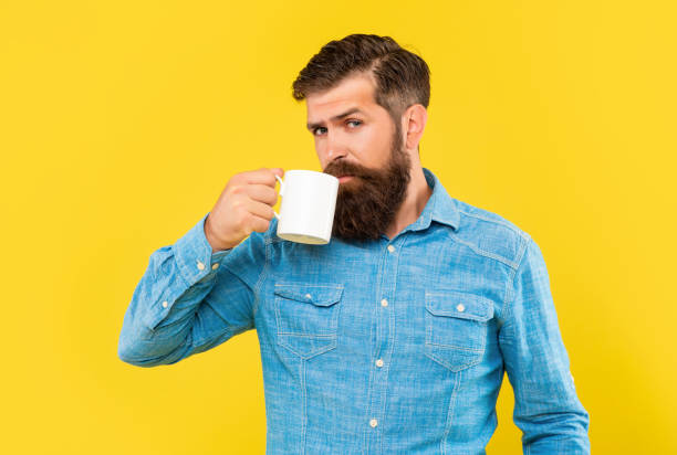 Serious caucasian guy drinking coffee from mug yellow background.