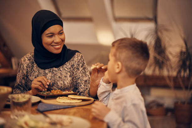 istock Smiling Muslim mother feeding her son while eating dinner at dining table. 1376090193
