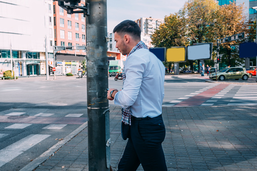 Young modern businessman is outside, walking in the city while looking around.