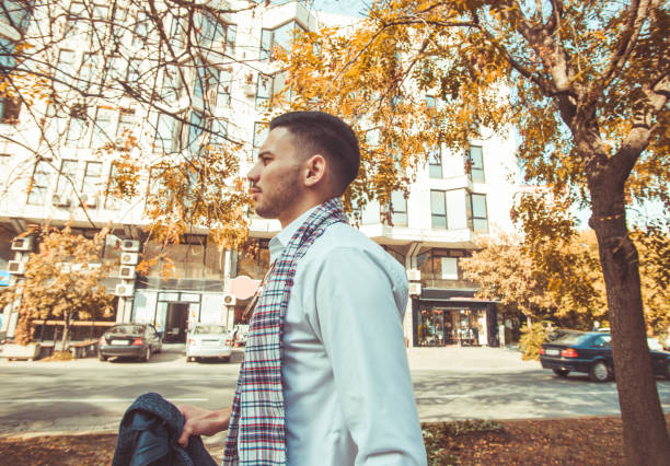 An attractive businessman is holding his coat in hand while enjoying and looking around the city buildings