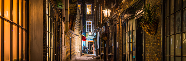 Warm lamplight illuminating a quiet narrow alleyway of higgledy piggledy houses at night in the heart of London, UK.