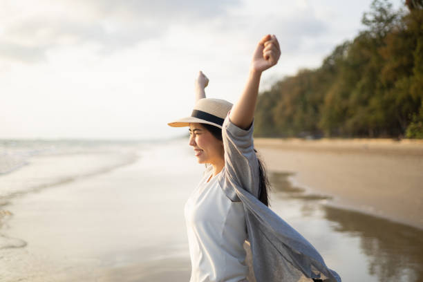 Beautiful asian woman stretching arm up into sky feeling happy at the beach with sunset. Take a break from work go on a trip. Woman travel in holiday weekend summertime. Relaxing in vacation time hermosa mujer asiática que estira el brazo hacia el cielo sintiéndose feliz en la playa con la puesta de sol. tómese un descanso del trabajo yéjese de viaje. mujer viaja en fin de semana de vacaciones de verano. relajarse en tiempo de vacaciones