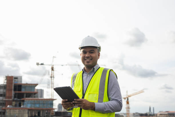 istock Asian engineer handsome man or architect use tablet with white safety helmet in city construction site . Standing on rooftop building construction at capital. 1376103376