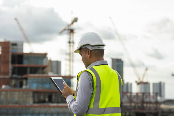 istock Asian engineer handsome man or architect use tablet with white safety helmet in city construction site . Standing on rooftop building construction at capital. 1376103426