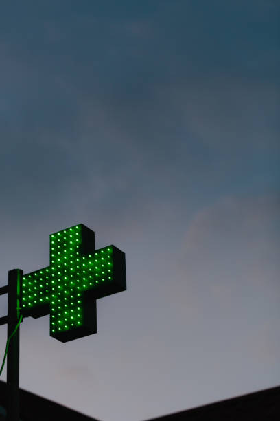 uma cruz de farmácia verde iluminada contra a escuridão nublada à noite - green cross - fotografias e filmes do acervo