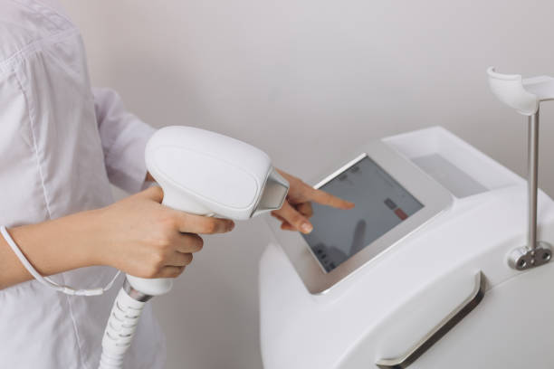 A woman tunes a laser hair removal machine. Girl holding a working part of the epilator in her hands in a modern beauty salon. Underarm Laser Hair Removal concept A woman tunes a laser hair removal machine. Girl holding a working part of the epilator in her hands in a modern beauty salon. Underarm Laser Hair Removal banner hair removal stock pictures, royalty-free photos & images