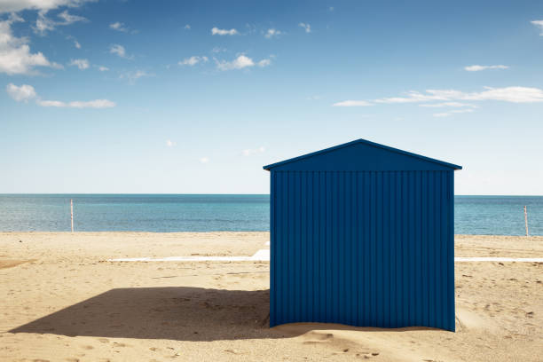 large blue shed on a sandy beach with the sea behind and a blue sky