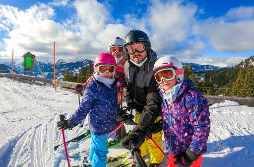 Family enjoying winter vacations taking selfie in skiing gear. Family with children on skiing vacation dressed in skiing gear with helmets and ski goggles on sunny day. Winter sports mountain resort.
