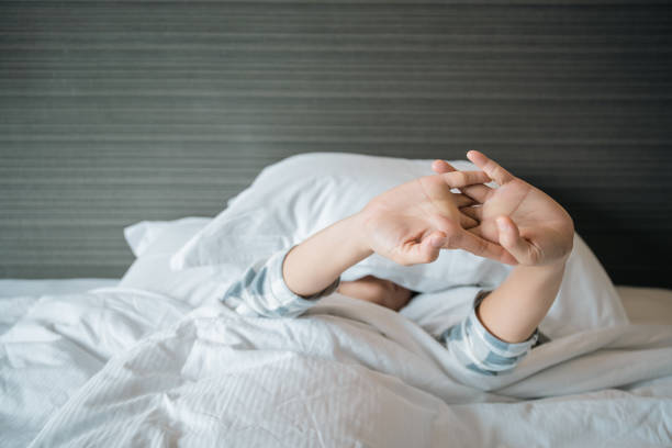 Close-up of human hand gripping a white blanket on soft bed, symbolizing comfort and relaxation.