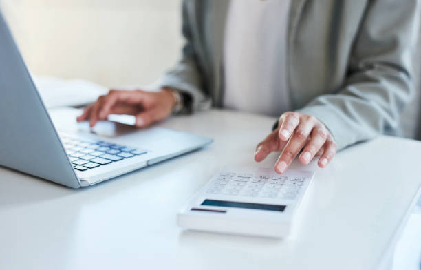 primer plano de una mujer de negocios irreconocible usando una calculadora y una computadora portátil en una oficina - salary fotografías e imágenes de stock