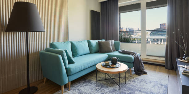 istock Creative composition of modern living room interior in small apartment. Eucalyptus sofa, black lamp, coffee table and personal accessories. Windows with a big city view on. Template. 1376168011