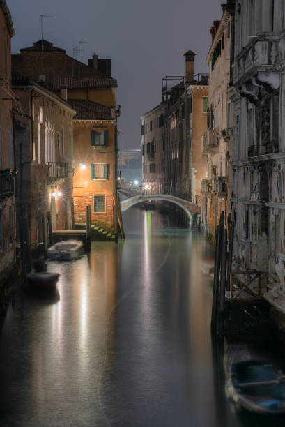 Night time in Venice and light trails from a small boat manoeuvre up a side canal towards the city's Grand Canal.