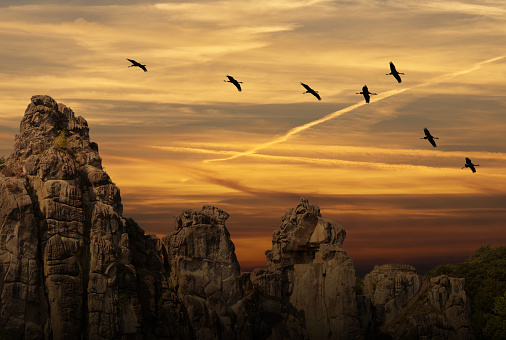 Evening sky with the silhouettes of migrating gray geese in the sky above a frightening rock formation