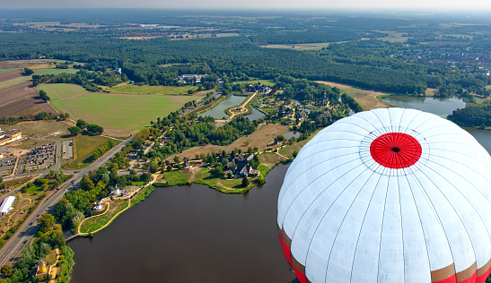 Aerial view over lake with mills and buildings on shore looking at top of flying balloon
